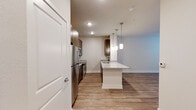 This thoughtfully designed single-floor residence offers a clean, modern aesthetic throughout. The open-concept layout connects the kitchen and living areas seamlessly, creating a bright and functional flow. The kitchen is a standout feature, equipped with stainless steel appliances including a refrigerator, range, and over-the-range microwave. Rich, dark-toned cabinetry provides ample storage and pairs elegantly with the speckled granite countertops. A subway tile backsplash adds a refined touch, while a central island with a built-in sink and pendant lighting above serves as both a prep space and a casual gathering point. Wood-look plank flooring runs consistently throughout the unit, contributing to a warm and cohesive feel. The living area is generously sized with neutral walls and recessed lighting, offering a versatile canvas for various furniture arrangements. A door with sidelight allows natural light to filter into the space. The bedroom areas are well-proportioned with clean lines, light-toned walls, and the same durable flooring. The bathroom features a granite-topped vanity with dark cabinetry, a framed mirror with overhead lighting, and a full tub-shower combination. Overall, the space presents a fresh, move-in-ready environment with consistent modern finishes.