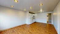 Located at 1701 12th Ave S in Seattle's Beacon Hill neighborhood, this one-bedroom, one-bathroom unit offers a practical and well-organized floor plan across a single level. The open-concept main living area seamlessly combines the living room, dining space, and kitchen into one cohesive zone. Warm hardwood-style flooring runs throughout this area, complemented by recessed ceiling lighting that provides even illumination throughout the space. The kitchen features white cabinetry, a full-size refrigerator, an electric range, and a built-in sink, all neatly integrated into the layout. A wall-mounted heater unit provides climate control in the living area. The bedroom is a well-proportioned room finished with plush carpeting and includes a dedicated closet for storage. Large windows allow natural light to fill the bedroom while offering views of the surrounding neighborhood. The bathroom is finished with hardwood-style flooring, a white vanity with under-cabinet storage, a framed mirror, and a lighted vanity fixture overhead. Clean white walls and consistent finishes throughout the unit create a bright, neutral aesthetic that is move-in ready and easy to personalize.