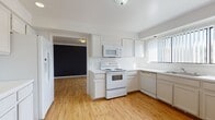 This two-floor residence offers a clean, functional layout with a variety of comfortable living spaces throughout. The kitchen is a standout area, outfitted with white cabinetry, white appliances including an electric range, built-in microwave, and dishwasher, all set atop warm light hardwood flooring. A large window dressed with vertical blinds fills the kitchen with natural light and provides outdoor views, creating a bright and welcoming atmosphere for cooking and dining.

The upper level features a carpeted hallway illuminated by an elegant brass chandelier, with a wrought iron stair railing adding a classic touch as it connects the two floors. The spacious carpeted living areas offer generous room for furnishing, with wide sliding glass doors in one room drawing in abundant natural light and offering access to outdoor views.

The bathrooms are finished in neutral tones with tile flooring, white vanities featuring ample counter space and under-sink storage, large mirrors, and enclosed glass-door showers. A dedicated laundry or utility room with tile flooring includes built-in shelving and cabinetry for added convenience.

Storage is well-considered throughout, with walk-in closets featuring built-in shelving and hanging rods. The overall palette of whites, creams, and warm neutrals lends the home a clean and airy ambiance across both levels.