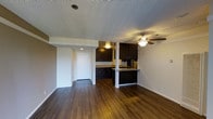 This single-floor space features an open layout that seamlessly connects the living area to the kitchen, creating a cohesive and functional environment. The flooring throughout is a rich, dark hardwood-style material that adds warmth and continuity across the space.

The kitchen is a standout feature, equipped with dark espresso-toned cabinetry that contrasts sharply against the light-colored walls and countertops. A peninsula with a breakfast bar provides additional seating and acts as a natural divider between the kitchen and the living area. The kitchen also benefits from under-cabinet lighting, enhancing visibility and ambiance during meal preparation.

The living area is open and well-proportioned, with a ceiling fan providing both light and air circulation. The textured ceiling adds a subtle design detail overhead. A hallway leads toward additional rooms, with a visible entry door featuring a clean, simple design.

The neutral wall tones throughout keep the space feeling bright and versatile, allowing for a variety of interior design choices. Overall, the layout is practical, with a straightforward flow that makes the space feel connected and easy to navigate.