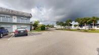Located at 1601 Northwest 13th Street in Boca Raton, Florida, this compact single-room space is part of a larger multi-building property in a well-established area of Palm Beach County. The exterior environment, visible from the property, features a spacious surface parking lot bordered by mature palm trees and tropical greenery characteristic of South Florida's landscape. The surrounding buildings are low-rise, two-story structures with balconies and a classic Florida architectural style, contributing to a relaxed, residential atmosphere. The property benefits from proximity to established infrastructure and a lush, green setting that is typical of the Boca Raton area. The interior space itself is modest in scale, comprising a single room on one level. Due to limited lighting in the interior imagery, specific finishes and fixtures are difficult to fully assess, though the space appears to include basic utilities. Its compact footprint makes it well-suited for use as a utility room, storage area, or similarly functional space. The overall setting reflects a quiet, tree-lined community environment with convenient access to the amenities of Boca Raton.