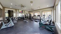 Located at 4101 Alta Towne Lake Cir in Pooler, GA, this single-floor fitness center is a comprehensively outfitted facility designed to support a wide range of workout routines. The space is divided into distinct functional zones, seamlessly connected through glass-paned doors that maintain an open, airy feel throughout.

The main workout area features durable rubber flooring and is lined with large windows on multiple walls, allowing abundant natural light to fill the room while providing pleasant outdoor views of the surrounding community grounds. Ceiling fans and recessed lighting ensure consistent comfort and visibility at any time of day.

The strength training section is well-stocked with a full rack of dumbbells spanning a wide weight range, multiple weight benches, and a multi-station cable machine for versatile resistance training. Wall-to-wall mirrors reflect the space and aid in form correction during exercise. Wall-mounted flat-screen televisions are positioned for easy viewing from multiple workout stations.

The cardio zone includes treadmills, elliptical machines, stationary bikes, and a stair-stepper, providing a comprehensive selection of aerobic equipment. An adjacent open area with light wood-look flooring offers a flexible space ideal for stretching, yoga, or mat-based exercises. The overall design of the facility is clean, modern, and functional, making it a well-rounded amenity for residents.