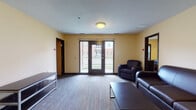 Located at 1482 N Lexington Springmill Rd in Mansfield, Ohio, this single-floor residential unit offers a functional and well-organized layout designed for shared living. The open living area is furnished with dark leather seating, a coffee table, and patterned carpet flooring, and features French doors that open to a private balcony with views of the surrounding building complex, allowing natural light to fill the space. A thermostat and ample wall space contribute to the room's practical design.

The kitchen is efficiently laid out in a galley style, equipped with light wood cabinetry, dark granite-style countertops, a white electric range, dishwasher, and a double sink. A breakfast bar with bar-height seating connects the kitchen to the living and dining area, where a dining table provides additional space for shared meals.

The bedrooms are comfortably sized, each featuring carpet flooring, a window with blinds for natural light and privacy, a twin bed frame, and a dedicated desk with chair — ideal for study or work. The textured ceilings and warm yellow accent walls carry throughout the unit, creating a cohesive aesthetic.

Multiple bathrooms serve the unit, each outfitted with a full tub-shower combination, a white vanity with sink, a large mirror, and tile flooring, offering clean and practical facilities for residents.