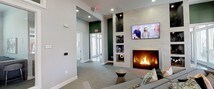 This single-floor amenity space is thoughtfully designed to serve as both a social and functional hub. The main lounge area centers around a marble-surround fireplace flanked by built-in display shelving, with a wall-mounted television above. Plush, neutral-toned sectional seating, accent pillows, and soft carpeting create a welcoming atmosphere, while a shuffleboard table and large windows providing natural light add to the relaxed yet refined ambiance. A bold green accent wall with an arched passage leads toward the entrance, adding a striking visual contrast to the light grey walls and recessed lighting throughout. Adjacent to the lounge, a glass-enclosed conference or co-working room offers a dedicated space for meetings, furnished with a long table and bar-height seating. A separate bar or social area features a dramatic textured tile accent wall, a deep navy high-top table surrounded by mixed upholstered bar stools, and eye-catching geometric pendant chandeliers that serve as a focal point. A wet bar with cabinetry and counter space completes the entertaining setup. Together, these areas form a cohesive, multi-functional community space designed for both relaxation and productivity.