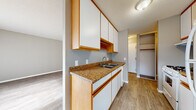 This single-floor unit offers a practical and cohesive layout, finished consistently with wood-look laminate flooring and neutral grey walls throughout. The galley-style kitchen is efficiently designed, featuring white cabinetry with warm wood trim, granite-look countertops, a double stainless steel sink, a white gas range, and a refrigerator. Upper cabinets provide generous storage, while a dedicated pantry/storage closet is accessible directly from the kitchen. The living area is bright and open, benefiting from a large floor-to-ceiling window with vertical blinds that allows substantial natural light. A wall-mounted air conditioning unit and baseboard heating ensure year-round comfort. A secondary room, suitable as a bedroom or additional living space, includes a window and baseboard heater. Additional bedrooms feature built-in closets with shelving and hanging rods, offering practical storage. One room includes a mirrored sliding closet. The full bathroom is straightforward and functional, equipped with a soaking tub and shower combination, a white vanity, and matching wood-trimmed cabinetry. The textured ceilings and clean white baseboards contribute to the unit's tidy, well-maintained presentation throughout.