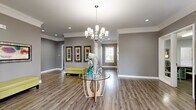 Located at 327 Prairie Pt in O'Fallon, Missouri, this single-story community clubhouse offers a well-appointed and thoughtfully designed space ideal for gatherings and everyday use. The entry area makes an immediate impression with warm hardwood-style flooring, crown molding, recessed lighting, and an elegant chandelier suspended above a glass-top accent table. Neutral gray walls carry throughout, lending the space a cohesive, modern aesthetic.

The open living room area features plush carpeting, large windows dressed with bold burnt-orange drapes, and a stacked stone accent wall, creating a comfortable and inviting atmosphere. Adjacent to the living space, the dining room offers flexible seating with access to French doors that open to an outdoor pool area, filling the room with natural light and outdoor views.

The kitchen is well-equipped with dark cabinetry, granite-style countertops, a dishwasher, and ample counter space. A breakfast bar with pendant lighting bridges the kitchen and gathering area, making it ideal for social occasions. A second kitchenette area serves as a convenient refreshment station.

The dedicated office, functioning as a business center, is outfitted with a workstation, printer, corkboard, and glass-panel door, providing a productive and private workspace. A hallway connects the various zones seamlessly throughout this generously sized community facility.
