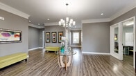 Located at 327 Prairie Pt in O'Fallon, Missouri, this single-story community clubhouse offers a well-appointed and thoughtfully designed space ideal for gatherings and everyday use. The entry area makes an immediate impression with warm hardwood-style flooring, crown molding, recessed lighting, and an elegant chandelier suspended above a glass-top accent table. Neutral gray walls carry throughout, lending the space a cohesive, modern aesthetic.

The open living room area features plush carpeting, large windows dressed with bold burnt-orange drapes, and a stacked stone accent wall, creating a comfortable and inviting atmosphere. Adjacent to the living space, the dining room offers flexible seating with access to French doors that open to an outdoor pool area, filling the room with natural light and outdoor views.

The kitchen is well-equipped with dark cabinetry, granite-style countertops, a dishwasher, and ample counter space. A breakfast bar with pendant lighting bridges the kitchen and gathering area, making it ideal for social occasions. A second kitchenette area serves as a convenient refreshment station.

The dedicated office, functioning as a business center, is outfitted with a workstation, printer, corkboard, and glass-panel door, providing a productive and private workspace. A hallway connects the various zones seamlessly throughout this generously sized community facility.