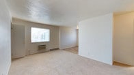 Located at 911 Randolph Street in Portsmouth, Virginia, this single-floor unit offers a straightforward and functional layout designed for comfortable everyday living. The main living area is finished with soft, neutral-toned carpeting that extends throughout, creating a warm and cohesive feel underfoot. The walls are painted in a clean, light neutral tone, contributing to a bright and airy atmosphere throughout the space. A large window in the living area allows natural light to fill the room, enhancing the open feel of the interior. Beneath the window, a wall-mounted HVAC unit provides convenient climate control, accompanied by a baseboard heating system along the perimeter for consistent warmth. The transition between the carpeted living space and an adjoining area with tile flooring adds a subtle visual distinction, suggesting a practical zone for dining or utility use. The smooth, light-toned ceiling completes the clean aesthetic of the interior. Overall, this unit presents a simple, well-maintained environment with essential features in place, making it a practical and move-in ready option in the Portsmouth, Virginia area.