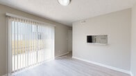 This two-floor residence offers a clean, neutral aesthetic throughout, with thoughtful design choices that create a bright and functional living environment. The main living area features light gray laminate flooring and soft beige walls, complemented by a textured ceiling. A full-width sliding glass door dressed with vertical blinds floods the space with natural light and provides direct access to an outdoor area, making the living room feel open and airy. A pass-through counter connects the living area to the kitchen, which is well-appointed with white shaker cabinets, granite-look countertops, a stainless steel sink, and a full suite of appliances including a refrigerator, electric range, and dishwasher. Light wood-style flooring continues through the kitchen, which also benefits from a skylight overhead. The bedrooms are located on the upper floor and are finished with plush carpeting in warm neutral tones. Each bedroom offers generous proportions, with windows that bring in natural light and closet space for storage. The bathrooms include a tiled shower-tub combination and a separate walk-in shower unit with chrome fixtures, offering both practicality and comfort. Throughout, consistent use of white trim and muted wall tones creates a cohesive and welcoming atmosphere.