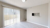 This two-floor residence offers a clean, neutral aesthetic throughout, with thoughtful design choices that create a bright and functional living environment. The main living area features light gray laminate flooring and soft beige walls, complemented by a textured ceiling. A full-width sliding glass door dressed with vertical blinds floods the space with natural light and provides direct access to an outdoor area, making the living room feel open and airy. A pass-through counter connects the living area to the kitchen, which is well-appointed with white shaker cabinets, granite-look countertops, a stainless steel sink, and a full suite of appliances including a refrigerator, electric range, and dishwasher. Light wood-style flooring continues through the kitchen, which also benefits from a skylight overhead. The bedrooms are located on the upper floor and are finished with plush carpeting in warm neutral tones. Each bedroom offers generous proportions, with windows that bring in natural light and closet space for storage. The bathrooms include a tiled shower-tub combination and a separate walk-in shower unit with chrome fixtures, offering both practicality and comfort. Throughout, consistent use of white trim and muted wall tones creates a cohesive and welcoming atmosphere.