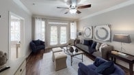 This single-floor residence combines thoughtful design with quality finishes to create a comfortable and stylish living environment. The living room serves as a welcoming centerpiece, featuring rich hardwood-style flooring, crown molding, a ceiling fan, and large French doors flanked by windows that flood the space with natural light and provide views of the outdoors. The adjacent dining area makes a bold statement with a dramatic dark accent wall, crown molding, and a pendant light fixture that anchors the room with an intimate, sophisticated atmosphere. The galley-style kitchen is efficiently designed with dark cabinetry, granite countertops, and full-size appliances, offering generous storage and counter space on both sides. A dedicated laundry area with a full-size washer and dryer is conveniently accessible off the kitchen. Both bedrooms are well-proportioned, featuring crown molding, ceiling fans, and large windows dressed with elegant curtains that invite natural light while maintaining privacy. The primary bathroom offers a granite-topped vanity with dark cabinetry, a framed mirror, and a shower-tub combination, while the secondary bathroom is clean and functional with a full tub-shower setup and white tile finishes. Throughout the residence, neutral tones and consistent design elements create a cohesive and polished aesthetic.