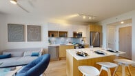 Located on Biscayne Boulevard in Miami's Upper Eastside neighborhood, this single-floor unit showcases a clean, contemporary design highlighted by light wood flooring, crisp white walls, and an abundance of natural light throughout. The open-concept living, dining, and kitchen area forms the heart of the space, where large floor-to-ceiling sliding glass doors lead to a private balcony offering sweeping views of Miami's green treetop canopy and city skyline beyond.

The kitchen is thoughtfully appointed with two-tone cabinetry combining warm wood and white finishes, a textured tile backsplash, stainless steel appliances including a French-door refrigerator, and a center island with a white quartz countertop that doubles as a dining and prep space. Track lighting overhead provides precise illumination throughout the area.

The bedroom features expansive floor-to-ceiling windows that frame lush outdoor views, flooding the room with natural light. Light wood flooring and minimalist furnishings contribute to a calm, airy atmosphere. The bathroom continues the design language with warm wood vanity cabinetry, white quartz countertops, and a backlit frameless mirror that enhances brightness. A ceiling fan circulates the warm Miami air throughout, completing this well-designed, light-filled urban retreat.