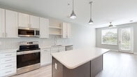 Located at 1020 E Broad St in Savannah, Georgia, this thoughtfully designed one-bedroom, two-bathroom residence offers a efficient yet comfortable single-floor layout with modern finishes throughout. The kitchen serves as the centerpiece of the home, showcasing crisp white shaker cabinetry, a hexagonal tile backsplash, and a full suite of stainless steel appliances including a French door refrigerator, electric range with over-the-range microwave, and dishwasher. A two-tone kitchen island with a clean white quartz countertop and charcoal gray base cabinetry provides additional storage and prep space, while two pendant lights hang above, adding a contemporary touch. Light wood-style flooring flows throughout the main living areas, complementing the neutral gray palette of the walls. The bedroom is a comfortable retreat featuring plush carpeting, natural light from a large window with blinds, a ceiling fan, and access to a walk-in closet outfitted with wire shelving. The bathrooms are clean and well-appointed, with white cabinetry, quartz countertops, and framed mirrors. The walk-in closet features hardwood-style flooring and ample wire rack storage. The overall ambiance is bright, clean, and move-in ready, reflecting a modern aesthetic well-suited to Savannah living.