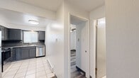 Located at 2032 Carlee Dr in Pueblo, Colorado, this two-bedroom, one-bathroom unit offers a practical and well-appointed single-floor layout. Throughout the living areas and bedrooms, durable wood-look luxury vinyl plank flooring in a neutral gray tone provides a cohesive and modern aesthetic, complemented by crisp white walls and textured ceilings.

The kitchen is equipped with dark gray cabinetry, a stainless steel dishwasher, and a window that allows natural light to filter in, creating a functional workspace. White tile flooring in the kitchen and bathroom provides a clean contrast to the rest of the unit.

The spacious primary bedroom is a standout feature, offering generous room to accommodate a variety of furniture arrangements. It includes a wall-mounted air conditioning unit, a baseboard heating system, and a wide window with horizontal blinds that bring in views of the surrounding neighborhood. A ceiling fan with integrated lighting is found in the second bedroom, which also features a window with blinds and baseboard heating.

The bathroom is finished with dark gray tile surrounding the tub-shower combination, white tile flooring, a gray vanity with an undermount sink, and brushed nickel fixtures. A hallway connects the rooms efficiently, with a closet accessible via a curtained entry rounding out the unit's storage options.