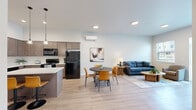 Located at 910 E Fourth Ave in Post Falls, Idaho, this one-bedroom unit offers a well-designed, single-level layout with a thoughtful blend of modern finishes and functional living spaces. The open-concept main area seamlessly connects the kitchen, dining, and living room, creating a bright and cohesive environment. The kitchen is a standout feature, equipped with warm taupe shaker-style cabinetry extending to the ceiling, white quartz countertops, a central island with bar seating, pendant lighting, black appliances including a refrigerator and electric range, and a dishwasher — providing ample storage and prep space. A wall-mounted mini-split system ensures efficient climate control throughout. Light wood-style flooring flows across the main living area, complementing the clean white walls and recessed lighting. The living room benefits from natural light through a large window and sliding patio door, which opens to an outdoor space. The bedroom is carpeted for comfort, features a generously sized closet with sliding doors, and includes a window for natural light. The unit offers a comfortable, contemporary living experience in a well-appointed residential community in Post Falls.
