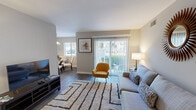 Located at 153 S Budding Ave in Virginia Beach, VA, this single-floor residence offers a thoughtfully designed layout with a welcoming and modern aesthetic throughout. The living room serves as the heart of the home, featuring dark hardwood-style flooring, neutral gray walls, and large sliding glass doors that flood the space with natural light and provide direct access to an outdoor patio with greenery views. A decorative sunburst mirror and patterned area rug add character to the room's clean, contemporary design. Adjacent to the living area, the dining space is defined by a round glass-top table beneath a dome pendant light, with a window framing outdoor views and adding to the airy feel. The galley-style kitchen is well-equipped with white shaker cabinets, granite countertops, a subway tile backsplash, stainless steel appliances including a gas range, microwave, and refrigerator, and light wood-style flooring. The primary bedroom features plush carpeting, a walk-in closet, and direct access to a private en-suite bathroom with white cabinetry. A second bedroom offers carpeted flooring, a bright window with natural light, and generous space. The residence combines functional design with stylish finishes, creating a comfortable and cohesive living environment throughout.