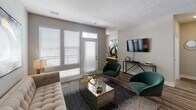 This single-floor residence offers a thoughtfully designed open-concept layout that seamlessly connects the main living spaces. The kitchen is a standout feature, outfitted with white shaker-style cabinetry, dark quartz countertops, a full suite of stainless steel appliances, a dark tile backsplash, and a large central island with bar seating and pendant lighting overhead — ideal for both cooking and casual dining. Wood-look flooring flows throughout the main living areas, lending warmth and continuity to the space.

The living room is bright and welcoming, benefiting from large windows and a glass-paneled door that invite generous natural light. The space is well-proportioned and well-suited for both relaxing and entertaining.

The primary bedroom features plush carpeting, a ceiling fan, and a window with sheer curtains that softens the incoming light. Its ensuite bathroom is finished with dark quartz countertops, white cabinetry, wood-look flooring, a large vanity mirror, and a walk-in closet with built-in shelving. A second bedroom offers similar comfort, with carpeting, a ceiling fan, and ample natural light. A second full bathroom mirrors the refined finishes found throughout the home, maintaining a cohesive and polished aesthetic.