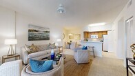 Located at 3884 Woodmere Park Blvd in Venice, Florida, this single-story residence offers a well-organized layout with comfortable living spaces throughout. The open-concept living and dining area forms the heart of the home, featuring soft carpeted flooring, a ceiling fan, and a sliding glass door that leads to a private outdoor patio, allowing natural light to fill the space. A large landscape-style artwork anchors the living area, adding a coastal touch to the warm, neutral palette.

The kitchen is positioned adjacent to the dining area and features warm wood cabinetry, white countertops, a double-basin sink, and a full suite of appliances including a refrigerator, dishwasher, and range. A skylight above the kitchen brings in additional natural light, and a breakfast bar with seating connects the kitchen to the main living space.

The two bedrooms are bright and generously sized, each with large windows offering views of the surrounding greenery and ceiling fans overhead. Both bathrooms are finished with tile flooring and warm wood vanities; one features a tub-shower combination, while the other is a half bath. A dedicated laundry area with side-by-side units provides added convenience. The overall ambiance is light, airy, and well-suited to Florida living.