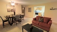 This single-floor residential space is designed with an open-concept layout that seamlessly connects the living, dining, and kitchen areas, creating a cohesive and functional environment. The living area is carpeted and anchored by a comfortable sofa and a dark-finished coffee table, offering a welcoming space for relaxation. A ceiling fan overhead provides both light and airflow, adding to the room's comfort.

Adjacent to the living area, the dining space accommodates a dark-toned dining table with matching chairs, making it well-suited for everyday meals or small gatherings. Wall art adds a decorative touch to the neutral, warm-toned walls that carry throughout the space.

The kitchen is accessible through an open archway and features light wood cabinetry, white appliances including a range and microwave, and ample counter space. The layout is efficient and practical, offering everything needed for home cooking. The open sightlines between the kitchen and living areas enhance the sense of spaciousness throughout the unit.

Overall, the space maintains a clean and straightforward aesthetic with neutral tones, plush carpeting, and a logical flow between rooms, making it a functional and comfortable place to call home.