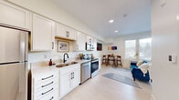 Located at 220 Quimby Street Northeast in Grand Rapids, Michigan, this efficiently designed studio offers a well-planned single-floor layout that makes intelligent use of its compact footprint. The open-concept living area seamlessly integrates the kitchen, dining, and sleeping zones into one cohesive space with a bright, airy feel enhanced by light-toned luxury vinyl plank flooring and recessed lighting throughout.

The kitchen is fully equipped with stainless steel appliances — including an electric range, built-in microwave, and dishwasher — complemented by crisp white shaker cabinetry with matte black hardware and a clean tile backsplash. A dedicated dining nook with a round table and seating sits adjacent to the kitchen, while the living and sleeping area features a sliding barn door that adds both a stylish architectural detail and functional room separation.

The bathroom is finished with a white vanity, open wood shelving, and a full shower with a curtained enclosure, continuing the clean, modern aesthetic found throughout the unit. A stacked washer and dryer unit is incorporated into the bathroom space, providing the convenience of in-unit laundry. Natural light filters in through a window overlooking the surrounding neighborhood. The overall design reflects a minimalist, contemporary style well-suited for efficient urban living.