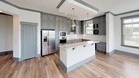 This single-floor residence on Providence Road in Charlotte, NC, presents a cohesive modern aesthetic carried throughout its thoughtfully designed layout. The open-concept living area features light wood-tone flooring, crisp white walls, gray accent trim, and large windows fitted with horizontal blinds that invite generous natural light and outdoor views.

The kitchen serves as a standout feature, showcasing floor-to-ceiling gray shaker-style cabinetry with polished chrome hardware, white quartz countertops, a subway tile backsplash, and a central island with seating. Stainless steel appliances, including a refrigerator with ice maker, wall oven, microwave, and cooktop, complement the space. A built-in wine cooler and dedicated wine rack add a refined touch.

The bedrooms feature plush neutral carpeting, ceiling fans, and windows offering natural light. Bathrooms are finished with marble-look tile flooring, gray cabinetry, white quartz vanity surfaces, chrome fixtures, and glass-enclosed showers. A dedicated laundry room accommodates a full-size washer and dryer with additional wire shelving for storage. The consistent use of gray trim, neutral tones, and quality finishes creates a polished, contemporary ambiance throughout.