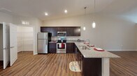 This single-floor residence offers a thoughtfully designed layout that balances functionality and comfort throughout its living spaces. The entryway welcomes residents with rich hardwood-style flooring and a windowed front door that invites natural light into the home.

The kitchen serves as a central highlight, featuring dark espresso Shaker-style cabinetry, granite countertops, and a full suite of stainless steel appliances including a refrigerator, range, microwave, and dishwasher. A peninsula with pendant lighting and an integrated sink adds both workspace and a casual dining option, while recessed ceiling lights brighten the area.

The living and dining areas extend from the kitchen, with hardwood-style flooring continuing underfoot and a sliding glass door that opens to outdoor views. Ceiling fans are present throughout the main living spaces, promoting comfort and airflow.

The bedrooms are carpeted and generously sized, each featuring ceiling fans, ample natural light from well-placed windows, and easy closet access. The bathrooms are finished with granite-topped dark vanities, large mirrors with bright vanity lighting, and shower areas with curtain enclosures. Hardwood-style flooring carries through the bathrooms, tying the home's aesthetic together cohesively.