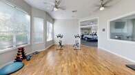 Located at 1500 Seagull Dr in Palm Harbor, Florida, this single-story fitness facility offers a comprehensive, well-appointed exercise environment spread across four dedicated exercise rooms. The layout is thoughtfully organized to accommodate a wide range of fitness activities.

The standout cardio room features a striking circular design with floor-to-ceiling windows that wrap around the space, flooding it with natural light and offering outdoor views. Treadmills, upright bikes, and ellipticals are positioned to take full advantage of this bright, airy atmosphere, complemented by ceiling fans and a wall-mounted TV.

An adjacent strength training area provides ample room for weight machines, a power rack, benches, and a full dumbbell rack, all set on durable rubberized flooring. Ceiling fans keep the space comfortable during intensive workouts.

A dedicated hardwood-floored studio serves as a versatile space for cycling classes, featuring spin bikes and a wall-mounted flatscreen TV, with additional room for stretching and group fitness. Exercise balls, mats, and other functional fitness accessories are neatly stored nearby.

Throughout the facility, white walls, abundant natural light from multiple windows, vaulted ceilings in select areas, and ceiling fans create a clean, modern, and energizing atmosphere well-suited for a variety of fitness routines.