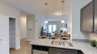 Located at 2821 Carolina Beach Rd in Wilmington, NC, this single-story space showcases a thoughtfully designed open-concept floor plan that seamlessly connects the kitchen, dining, and living areas. The kitchen serves as a central hub, featuring granite countertops with an undermount double-basin sink, dark cabinetry, and a built-in dishwasher. A kitchen island provides both additional workspace and casual seating, while two elegant pendant lights with brushed nickel fixtures hang overhead, adding a polished touch to the space.

The open layout flows naturally into the living and dining areas, where light-toned luxury vinyl plank flooring runs throughout, contributing to a clean and cohesive aesthetic. The living area is bright and inviting, benefiting from natural light that pours in through a set of French doors, which also provide a view of the outdoors. Neutral gray walls complement the light flooring, creating a versatile backdrop. The space is finished with standard ceiling heights and recessed lighting that ensures consistent illumination throughout, making the overall ambiance feel warm, functional, and modern.
