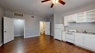 This efficient single-floor studio offers a well-organized layout that maximizes every square foot. The open-concept main area seamlessly integrates the kitchen and living room, creating a flexible and functional living space. Rich, warm-toned hardwood-style flooring runs throughout the entire unit, providing a cohesive and inviting aesthetic. A ceiling fan centered in the main area promotes airflow and comfort year-round.

The kitchen is outfitted with white cabinetry — including both upper and lower cabinets with open shelving — a full-size refrigerator, an electric range with oven, a dishwasher, and a single-basin sink. A window adjacent to the kitchen allows natural light to brighten the cooking area. The living room portion benefits from multiple windows along the front wall, filling the space with natural light and offering views of the exterior.

The bathroom is finished in a neutral gray palette with wood-look flooring, and includes a bathtub, toilet, vanity sink, towel bar, and a storage rack — all cleanly appointed. A separate closet with built-in shelving provides dedicated storage. Gray-toned walls and white trim throughout the unit create a clean, modern, and move-in ready feel.