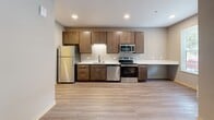 Located at 424 W Mifflin St in Madison, Wisconsin, this efficiently designed single-floor unit offers a well-organized layout that maximizes its compact footprint. The open living area features wood-look plank flooring and neutral-toned walls, creating a clean and contemporary aesthetic throughout.

The kitchen is a standout feature, outfitted with rich, dark-stained wood cabinetry, white countertops, and a full suite of stainless steel appliances including a refrigerator, electric range, built-in microwave, and dishwasher. Recessed lighting illuminates the space, and the open design connects the kitchen naturally to the living area.

A dedicated workspace is thoughtfully integrated into the unit, featuring a built-in white desk surface with wood cabinetry below, accompanied by a window that brings in natural light — a practical feature for residents working or studying from home.

The bathroom is finished to a modern standard, with a dark wood vanity, white countertop with an undermount sink, a large mirror, and wood-look tile flooring. A walk-in shower completes the bathroom's clean, functional design.

Throughout the unit, consistent use of warm wood tones and neutral gray walls lends a cohesive and polished feel, making this a practical and stylish space in the heart of Madison.
