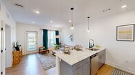 Located in Huntsville, Alabama, this well-appointed one-bedroom, one-bathroom unit offers a smartly designed single-floor layout that maximizes every square foot. The open-concept kitchen is a standout feature, boasting warm wood cabinetry, stainless steel appliances, and a granite-topped peninsula with bar seating, illuminated by stylish pendant lighting. Light wood-style flooring flows seamlessly throughout the space, lending a cohesive and modern aesthetic. The living room is bright and airy, featuring multiple windows dressed with elegant teal drapes and sheer curtains that invite abundant natural light and outdoor views. The spacious primary bedroom offers a ceiling fan, a large window with outdoor views, and convenient access to both a dedicated closet and the full bathroom. The bathroom is clean and contemporary, featuring a full tub-shower combo with a curved rod, a stone-topped vanity with a blue cabinet, and built-in shelving for storage. Throughout the unit, crisp white walls, clean lines, and modern black hardware accents create a fresh, cohesive design. The thoughtful layout and quality finishes make this unit a comfortable and stylish place to call home.