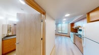 Located at 1801 E Yesler Way in Seattle's vibrant Capitol Hill neighborhood, this efficiently designed unit makes smart use of its compact footprint across a single floor. Light wood flooring runs throughout the space, creating a warm, cohesive aesthetic that ties each area together seamlessly.

The kitchen is well-appointed with warm-toned wood cabinetry extending floor to ceiling, offering generous storage. It includes an electric range with overhead ventilation, a stainless steel sink, ample counter space with gray laminate surfaces, and a full-size refrigerator — providing all the essentials for everyday cooking.

The main living area benefits from large windows fitted with vertical blinds, allowing natural light to fill the room while offering views of the surrounding Seattle cityscape and treetops. Recessed lighting supplements the natural light, keeping the space bright and welcoming.

Two bathrooms serve the unit, one of which features a wide vanity with wood cabinetry, a stone-tone countertop, dual mirrors, and accessibility grab bars — reflecting a thoughtful, functional design. A sliding wood-panel door adds a modern, space-saving touch to the interior layout.

Overall, the unit presents a clean, contemporary design with warm wood accents, practical finishes, and a well-organized layout suited for efficient urban living in Seattle.
