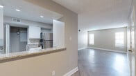 This single-floor residence offers a clean, modern aesthetic defined by a cohesive neutral color palette, crisp white trim, and distinctive herringbone-patterned luxury vinyl flooring that flows consistently throughout the space. The open-concept living and dining area is bright and welcoming, with natural light filtering in through blinded windows and a front entry door that anchors the main living space.

The kitchen is thoughtfully designed with white shaker-style cabinetry, granite countertops, a herringbone tile backsplash, and a full suite of stainless steel appliances including a refrigerator, range, and over-the-range microwave. A pass-through counter connects the kitchen to the living area, enhancing the sense of openness and facilitating easy interaction between spaces.

A hallway leads to the bedrooms, each featuring herringbone flooring, ceiling fans, and reach-in closets with built-in shelving. The rooms are generously proportioned and receive ample natural light through large windows. The bathroom continues the design language of the home, with granite-topped white vanity cabinetry, a tiled tub-shower combination, and coordinating herringbone flooring. Textured ceilings add subtle dimension throughout, completing a polished and move-in-ready interior.