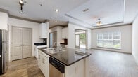 Located at 2910 Clairmont Rd in Atlanta, Georgia, this single-floor residence offers a thoughtfully designed open-concept layout that seamlessly connects the kitchen and living areas. The kitchen is a standout feature, equipped with a curved granite-topped island with a built-in sink, white shaker-style cabinetry extending to the ceiling, a dark subway tile backsplash, and a full suite of stainless steel appliances including a range, microwave, and refrigerator. Wood-style flooring runs throughout the main living areas, complementing the clean, modern aesthetic. The spacious living room is defined by an elegant tray ceiling with crown molding detail and a ceiling fan, while large windows and glass French doors flood the space with natural light and provide direct access to a private outdoor balcony with lush tree views. The bedroom features plush carpet flooring, a ceiling fan, and a generous walk-in closet outfitted with wire shelving on multiple walls for ample storage. The bathroom includes a tiled tub-surround combination, granite vanity countertop, and light tile flooring. Track lighting and recessed fixtures provide versatile illumination throughout the unit, creating a bright and welcoming ambiance.