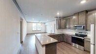 Located in League City, TX, this single-story, 2-bedroom, 2-bathroom residence offers a thoughtfully designed layout with modern finishes throughout. The open-concept kitchen and living area serves as the heart of the home, featuring rich, dark-stained wood cabinetry, granite countertops, a subway tile backsplash, and stainless steel appliances including a range, microwave, and refrigerator. A large kitchen island with an integrated sink and pendant lighting provides additional prep space and a casual dining option, flowing seamlessly into the living area. Wood-style plank flooring runs throughout the home, adding warmth and continuity. Crown molding accents the common areas, enhancing the clean, contemporary aesthetic. Both bedrooms are well-sized, filled with natural light from multiple windows, and equipped with ceiling fans. The spacious primary bedroom includes a generous walk-in closet with wire shelving. The primary bathroom is appointed with a dual-sink granite vanity, a large framed mirror, and a tub-shower combination. A private balcony off the living area offers outdoor views of the landscaped surroundings and open sky. A dedicated hallway and two closets provide practical storage throughout the residence.