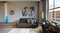 Located at 119 E Third St in the heart of downtown Dayton, Ohio, this thoughtfully designed unit blends contemporary style with urban character. The entry welcomes you with elegant marble-look tile flooring and a rich wood door accented by brass hardware, setting a refined tone from the start.

The open-concept kitchen is a standout feature, showcasing high-gloss gray cabinetry that extends to the ceiling, a geometric hexagonal tile backsplash, stainless steel appliances, and a generous waterfall-edge island with seating for multiple guests, illuminated by sleek pendant lighting. The kitchen flows seamlessly into the expansive living area, where wide-plank hardwood-style flooring, soaring ceilings, and exposed industrial elements nod to the building's heritage.

Large windows in the living room frame sweeping views of the downtown Dayton skyline, flooding the space with natural light. The living area is complemented by curated contemporary furnishings and artwork.

The bedrooms offer a calm retreat, featuring tall ceilings, soft neutral tones, and quality finishes. High interior windows allow additional light while maintaining privacy.

The bathroom is appointed with large-format marble-look tile flooring, a floating gray vanity, a backlit mirror, and a sleek walk-in shower, delivering a spa-inspired experience. This urban residence masterfully combines modern design with the vibrant energy of downtown Dayton.