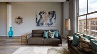 Located at 119 E Third St in the heart of downtown Dayton, Ohio, this thoughtfully designed unit blends contemporary style with urban character. The entry welcomes you with elegant marble-look tile flooring and a rich wood door accented by brass hardware, setting a refined tone from the start.

The open-concept kitchen is a standout feature, showcasing high-gloss gray cabinetry that extends to the ceiling, a geometric hexagonal tile backsplash, stainless steel appliances, and a generous waterfall-edge island with seating for multiple guests, illuminated by sleek pendant lighting. The kitchen flows seamlessly into the expansive living area, where wide-plank hardwood-style flooring, soaring ceilings, and exposed industrial elements nod to the building's heritage.

Large windows in the living room frame sweeping views of the downtown Dayton skyline, flooding the space with natural light. The living area is complemented by curated contemporary furnishings and artwork.

The bedrooms offer a calm retreat, featuring tall ceilings, soft neutral tones, and quality finishes. High interior windows allow additional light while maintaining privacy.

The bathroom is appointed with large-format marble-look tile flooring, a floating gray vanity, a backlit mirror, and a sleek walk-in shower, delivering a spa-inspired experience. This urban residence masterfully combines modern design with the vibrant energy of downtown Dayton.
