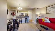 This single-floor residence offers a thoughtfully designed open-concept layout that seamlessly connects the living, dining, and kitchen areas. The living room is a comfortable and inviting space, featuring plush carpeting, large windows, and a sliding glass door that opens onto a private balcony overlooking lush, tree-lined surroundings — bringing in natural light and peaceful outdoor views.

The kitchen is well-equipped with stainless steel appliances, including a refrigerator, range, and over-the-range microwave, complemented by white cabinetry, dark countertops, and light hardwood-style flooring. A breakfast bar with bar stool seating bridges the kitchen and dining area, where a pendant chandelier adds a stylish focal point above the dining table.

The residence includes two bedrooms, each carpeted and featuring windows that allow natural light to filter in. One bedroom offers direct access to the balcony through a sliding door, along with a closet for ample storage. The bathroom is clean and functional, outfitted with hardwood-style flooring, a full tub and shower combination, and neutral wall tones. Throughout the home, warm beige walls and consistent finishes create a cohesive and comfortable living environment.