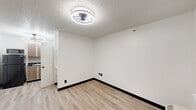 This single-floor unit located at 14255 Northwest Fwy in Houston, TX, offers a clean, functional layout with consistent design elements throughout. Light wood-style vinyl flooring flows across the main living and sleeping areas, complemented by crisp white walls, black baseboards, and textured ceilings. Circular flush-mount light fixtures provide consistent overhead illumination throughout the space.

The main living area is open and versatile, featuring a front entry door with an adjacent window and a wall-mounted HVAC unit for climate control. Multiple electrical outlets are positioned throughout for added convenience. The space transitions naturally into a compact kitchenette area, which includes light wood cabinetry, a sink, a full-size black refrigerator, and a microwave, all accented by a sputnik-style pendant light fixture.

A separate room provides a defined sleeping or multipurpose area with its own ceiling fan and ample wall space. Built-in shelving is accessible nearby, offering practical storage. The bathroom features a soaking tub enclosed by striking floor-to-ceiling marble-patterned tile surrounds in white and grey tones, creating an elegant focal point within an otherwise straightforward layout. Overall, the unit presents a tidy, updated interior suited for functional everyday living.