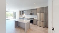 This well-appointed two-story home offers four bedrooms, two bathrooms, and multiple living spaces spread across two thoughtfully designed floors. The ground floor provides a generous footprint encompassing the main living and kitchen areas, while the upper floor houses the private quarters.

The contemporary kitchen is a standout feature, showcasing wood-grain cabinetry in a warm gray-taupe finish, white quartz countertops, a classic subway tile backsplash, and a full suite of stainless steel appliances including a gas range, dishwasher, microwave, and refrigerator. A central island adds additional prep and gathering space, and the kitchen flows seamlessly into the open living area, which is bathed in natural light from large floor-to-ceiling windows and sliding glass doors.

The bedrooms feature light wood-style flooring, clean white walls, and generous windows — some with sliding glass doors that open to street-facing views. The primary bedroom is a comfortable retreat with access to a dedicated walk-in closet featuring multi-rod hanging storage and shelving. The bathrooms are finished in a clean, modern style with white tile surrounds, soaking tub-shower combos, and dark-accented vanities with quartz counters. Light wood flooring runs throughout, tying the home's bright, contemporary aesthetic together cohesively.