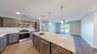 Located at 4795 Park Place Dr in Fort Wayne, Indiana, this single-floor residence offers a thoughtfully designed layout with two bedrooms, two bathrooms, and two closets. The open-concept kitchen and living area serves as the heart of the home, anchored by a large granite-topped island with an integrated sink and pendant lighting overhead. Dark-toned cabinetry, a tiled backsplash, and stainless steel appliances complete the kitchen, which flows seamlessly into the living room. The living room features rich hardwood-style flooring, a ceiling fan, and a sliding glass door that opens to a private balcony with outdoor views of green surroundings. The primary bedroom is generously sized, finished with plush carpeting and a ceiling fan, and connects directly to an en-suite bathroom featuring a granite vanity with dark cabinetry and a walk-in closet equipped with wire shelving. The second bedroom also benefits from natural light via a window with outdoor views, soft carpeting, and its own ceiling fan. The second bathroom mirrors the same quality finishes, with a granite countertop vanity, hardwood-style flooring, and access to an adjacent closet. Throughout, neutral tones and clean lines create a bright, modern ambiance.