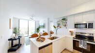 Located at 2585 Spruce Ave in West Palm Beach, FL, this well-appointed two-bedroom, two-bathroom residence offers a thoughtfully designed single-level layout filled with natural light and modern finishes throughout. Light-toned hardwood-style flooring flows continuously across the entire home, creating a cohesive and airy feel.

The open-concept kitchen is a standout feature, showcasing sleek white cabinetry extending to the ceiling, a quartz waterfall island with bar seating, stainless steel appliances, and open shelving for display. It connects seamlessly to the living area, which is anchored by large sliding glass doors leading to a private balcony with expansive views of the surrounding West Palm Beach skyline and lush tree canopy.

The spacious primary bedroom includes a walk-in closet and large windows that frame scenic outdoor views, while a ceiling fan ensures year-round comfort. The second bedroom is equally well-lit, with its own generous window and ceiling fan. Each bathroom is finished in a clean, contemporary style — one featuring a full tub-shower combo and built-in wall niche, the other a frameless glass walk-in shower — both with crisp white tile and wood-look flooring.
