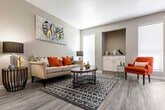 This single-floor residence offers a thoughtfully designed open-concept layout that connects the living, dining, and kitchen areas into one cohesive and functional space. The living room features durable wood-look flooring, neutral-toned walls, and abundant natural light streaming through large windows with blinds. A built-in niche with white cabinetry and a granite-style countertop serves as a distinctive architectural accent. The galley-style kitchen is equipped with white shaker cabinetry, granite-look countertops, a stainless steel range, and a pass-through counter that opens toward the dining area—ideal for entertaining. The dining space accommodates a round table and benefits from sliding glass door access to an outdoor area. Both bedrooms are carpeted and include ceiling fans, ample closet space, and generous natural light from well-placed windows. The primary bedroom connects directly to a laundry area for added convenience. The bathrooms are finished with wood-look flooring, white cabinetry, granite-style vanity countertops, and a tiled tub-shower combination. Clean lines, consistent neutral tones, and practical built-in storage throughout give this residence a cohesive, comfortable character suited for everyday living.