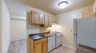 This single-floor residence offers a practical and well-organized layout designed for comfortable everyday living. The kitchen is equipped with light oak cabinetry providing ample upper and lower storage, dark laminate countertops, a double-basin sink, a gas range, a dishwasher, and a refrigerator. Neutral-toned walls and tile flooring give the kitchen a clean, functional appearance, while an adjacent alcove offers additional utility space.

The bathroom features white subway tile wainscoting, a single-sink vanity with an oak cabinet base, a white countertop, a medicine cabinet with a mirrored door, and tile flooring — delivering a tidy and efficient design.

The living area is generously proportioned, with plush wall-to-wall carpeting and large sliding glass doors fitted with vertical blinds that invite natural light and offer views of outdoor greenery. The open layout flows seamlessly between the living and dining areas, creating a bright and airy atmosphere.

The bedrooms are carpeted and well-sized, each featuring neutral walls and ample natural light from windows. At least one bedroom includes direct access to a dedicated closet space. A carpeted hallway connects the bedrooms to the main living areas, completing the efficient and cohesive floor plan.