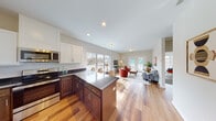 This single-floor residence offers a thoughtfully designed open-concept layout that seamlessly connects the kitchen, dining, and living areas. The kitchen is a standout feature, boasting two-tone cabinetry with crisp white upper cabinets and rich dark wood lower cabinets, dark granite countertops, a classic subway tile backsplash, and a full suite of stainless steel appliances including a range, microwave, and dishwasher. A central island with granite countertop provides additional prep space and casual seating. Warm hardwood flooring flows throughout the main living areas, enhancing the bright, airy atmosphere created by abundant natural light streaming through large windows and sliding glass doors. The living area is generously proportioned, with direct access to an outdoor space. The bedroom offers a comfortable retreat with plush carpeting, a large window, and neutral walls. A bathroom features tile flooring, a wood vanity with granite countertop, and clean, modern fixtures. The overall ambiance is contemporary and welcoming, with a neutral color palette and consistent high-quality finishes that lend a cohesive, polished feel throughout the entire space.