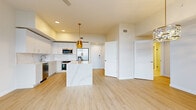 Located at 301 Third St S in the heart of downtown Saint Petersburg, Florida, this single-floor residence presents a contemporary design defined by clean lines, upscale finishes, and an abundance of natural light. The open-concept layout connects the living and dining areas seamlessly, with light wood-tone flooring running throughout the main living spaces and elegant gold-toned pendant and chandelier light fixtures adding warmth and visual interest.

The kitchen is a standout feature, outfitted with white shaker-style cabinetry adorned with brushed gold hardware, a striking marble-look quartz backsplash, and matching quartz countertops extending across a central island. Stainless steel appliances—including a refrigerator with ice maker, wall oven, microwave, dishwasher, and a built-in wine cooler—complete this highly functional culinary space.

The bedrooms feature plush carpeting and ceiling fans, with at least one room benefiting from dramatic floor-to-ceiling windows that frame sweeping views of the surrounding Saint Petersburg cityscape. Walk-in closet space provides ample storage. The bathroom is finished with large-format tile flooring, a quartz vanity with gold-hardware cabinetry, and a glass-enclosed walk-in shower with white subway tile. Throughout, the space maintains a bright, refined, and modern ambiance.