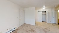 Located on Wingate Drive SE in Kentwood, Michigan, this single-floor unit offers a straightforward and functional layout well-suited for comfortable everyday living. The living area is generously proportioned, featuring neutral-toned wall-to-wall carpeting, a textured ceiling, and a long baseboard heater that spans much of the exterior wall. A sliding glass door allows natural light to fill the space and provides access to the outdoors. The entryway area includes a built-in closet with bifold doors, offering convenient storage right at the front door. The galley-style kitchen is efficiently designed with ample upper and lower cabinetry in a light wood-accented finish, a gas range, a full-size refrigerator, a stainless steel double sink, and tile flooring that adds durability underfoot. The bedroom is a comfortable, well-lit room featuring carpet, a window with outdoor views of surrounding greenery, and its own baseboard heating unit. The full bathroom is cleanly appointed with a single-sink vanity, a wall mirror, a toilet, and a tub-shower combination with tiled surround. Throughout the unit, the neutral color palette and consistent finishes create a cohesive and move-in-ready environment.