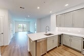 This well-appointed 2-bedroom, 2-bathroom residence offers a thoughtfully designed single-level layout that balances comfort and modern style. The open-concept kitchen and living area serves as the heart of the home, featuring a large central island with a crisp white quartz countertop, undermount sink, and a pull-down faucet. Gray shaker-style cabinetry lines the kitchen walls, complemented by stainless steel appliances including a gas range, built-in microwave, French door refrigerator, dishwasher, and a built-in wine cooler. Recessed lighting illuminates the space throughout, while light-toned hardwood flooring flows seamlessly across all living areas. The living room opens to a private balcony through sliding glass doors, offering pleasant outdoor views. Both bedrooms are clean and bright, featuring the same warm hardwood flooring and neutral white walls that lend a versatile, move-in-ready feel. The two bathrooms are finished with gray tile flooring; one features a soaking tub with a full tile surround, while the other offers a glass-enclosed walk-in shower with brushed gold hardware and warm wood cabinetry. A hallway and closet complete the layout, adding practical storage to this polished, contemporary residence.
