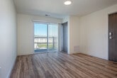 This thoughtfully designed single-floor unit offers a clean, modern aesthetic anchored by light wood-tone flooring that flows seamlessly throughout the entire space. The open-concept kitchen serves as the centerpiece, featuring rich dark wood cabinetry, light quartz countertops, a large peninsula with pendant lighting overhead, and a full suite of stainless steel appliances including a range, dishwasher, built-in microwave, and refrigerator. Recessed lighting and a dedicated range hood complete the kitchen's polished, functional look.

The living and bedroom areas are bright and airy, benefiting from large windows that invite generous natural light and offer views of the surrounding neighborhood. One room features a sliding glass door that opens directly to a private balcony, extending the living space outdoors.

The bathroom is clean and well-appointed, with a full soaking tub and shower combination, a vanity with dark wood cabinetry and a white countertop, and wood-look flooring that ties in with the rest of the unit. A spacious walk-in closet with wire shelving provides ample storage, while a dedicated in-unit laundry area houses a stacked washer and dryer for added convenience. The overall ambiance is bright, contemporary, and move-in ready.
