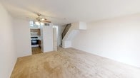 This two-floor residence offers a practical and comfortable layout spread across two well-organized levels. The main floor features a spacious living area finished with warm beige carpeting and a ceiling fan with integrated lighting. A staircase with a metal railing connects to the upper level, while an adjacent kitchen is equipped with oak cabinetry, white countertops, a coil-burner range with oven, and a ventilation hood — offering ample storage and prep space. A sliding glass door on the main level fills the space with natural light and provides access to an outdoor area. The upper level hosts multiple bedrooms, each carpeted and featuring windows that allow in natural light. A standout bedroom includes two generous closets fitted with hanging rods and shelving, offering excellent storage capacity. Additional bedrooms are well-proportioned with neutral walls and window blinds. The full bathroom is clean and functional, featuring a single-sink vanity with a wood cabinet base, a mirrored medicine cabinet with overhead lighting, and a full-size tub and shower combination. Throughout the home, the neutral color palette and consistent carpeting create a cohesive, move-in ready environment.